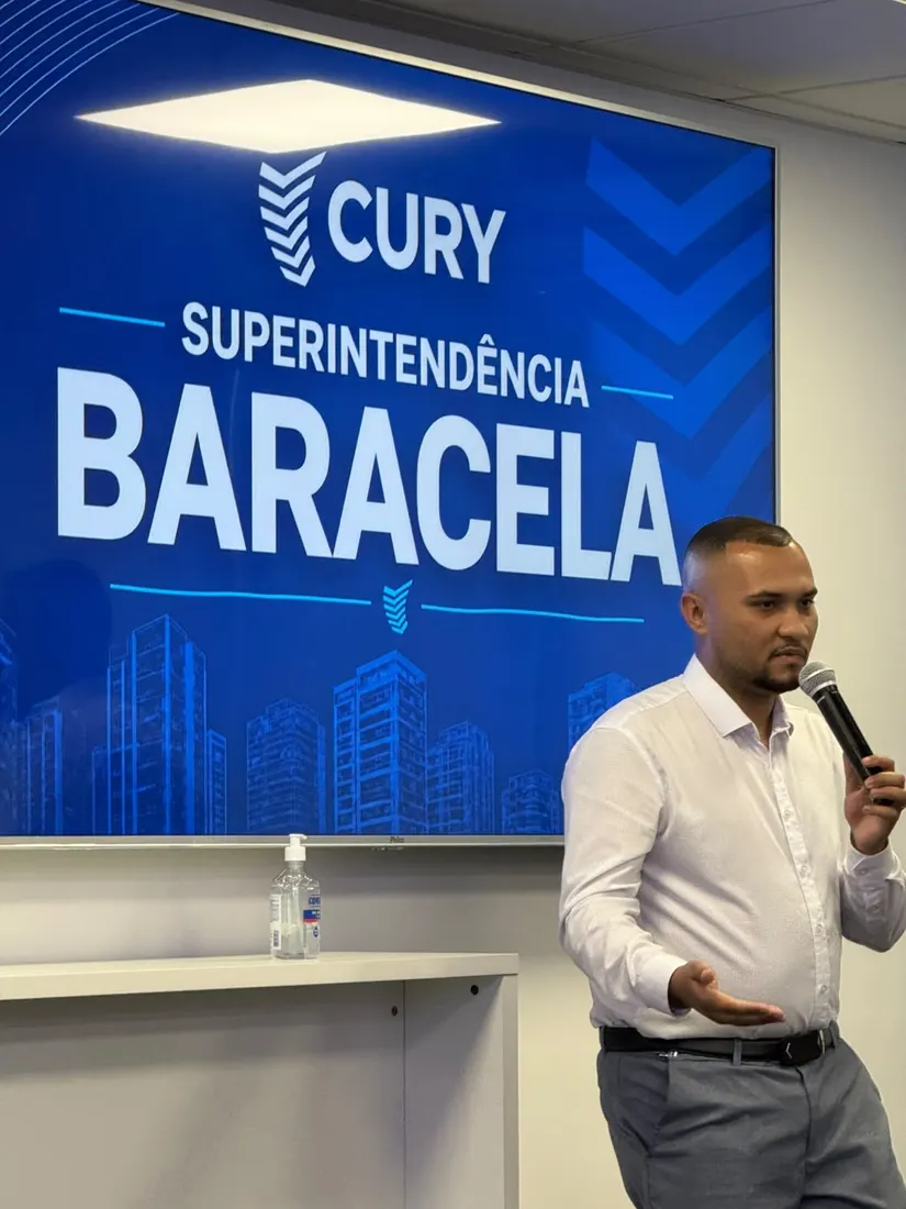 Ricardo Baracela falando ao microfone diante do telão Cury Superintendência Baracela